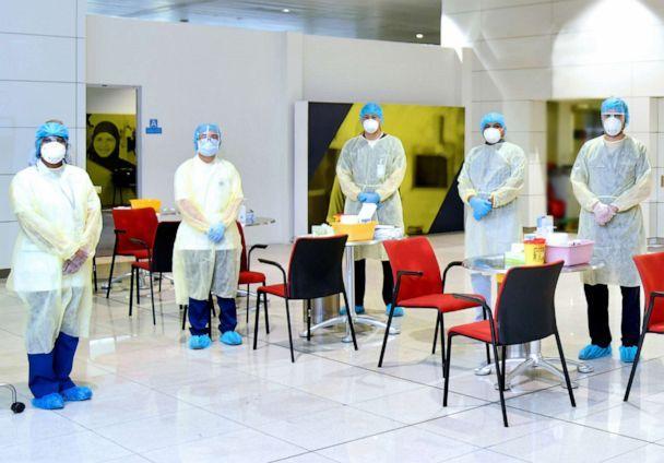 medical staff dressed in PPI in the airport around tables and chair to test passengers for COVID