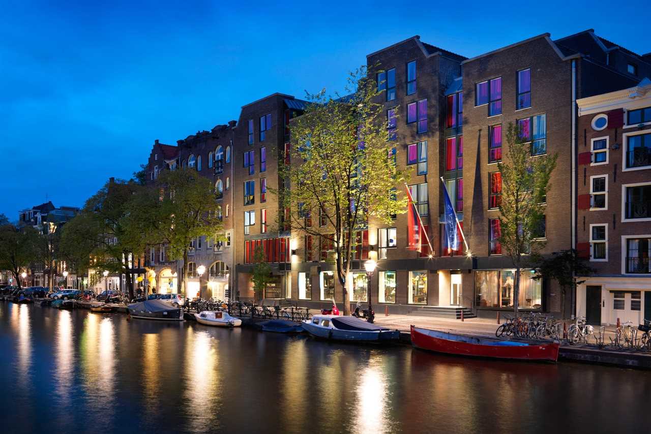 canal in Amsterdam with boats, bikes and row of beautiful houses at night