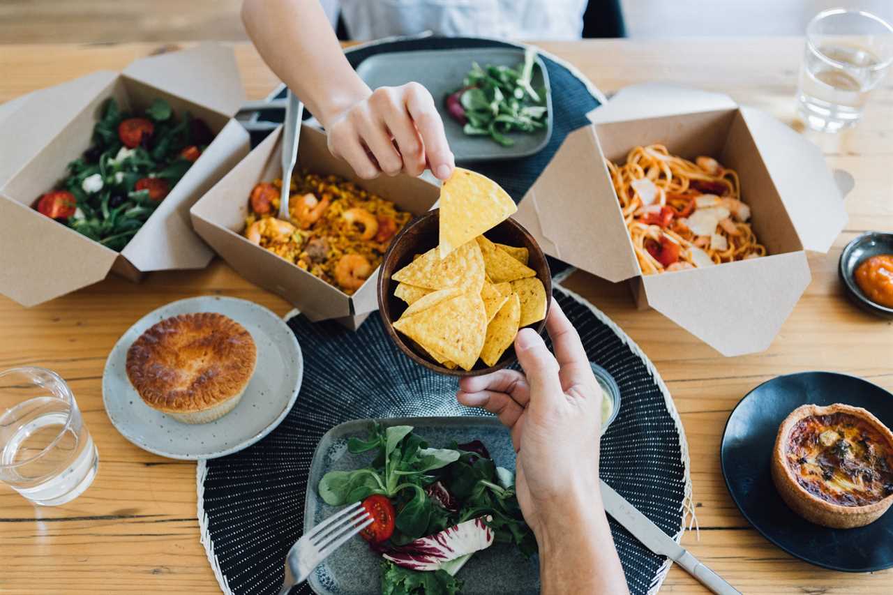 Personal perspective view of couple sharing Tortilla chips while eating takeaway food together at the dining table.