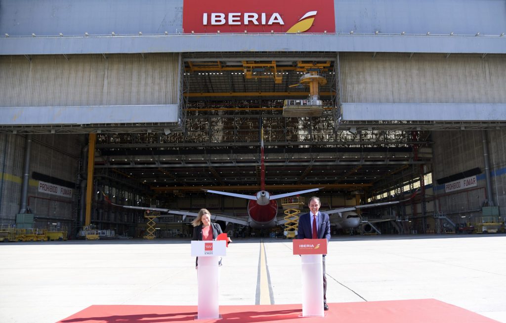 President of Iberia signs agreement with Councillor of Community of Madrid in front of large aircraft storage.