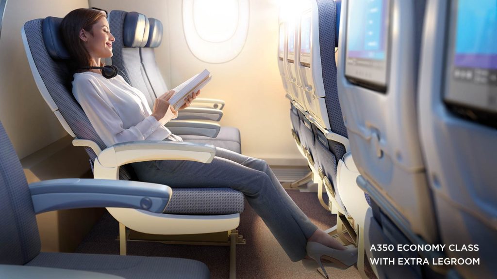 Visual of woman sitting in cabin with extra legroom, smiling as she reads a book.