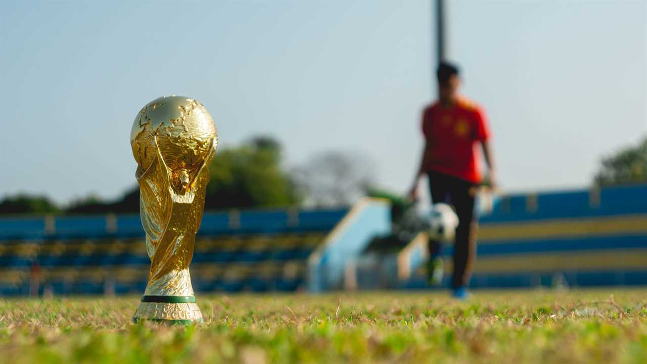 A footballer stands blurred out behind the World Cup trophy