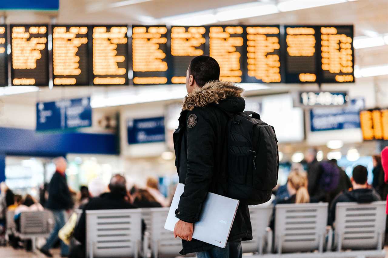 Man carries a laptop through the airport as he scans the flight information board