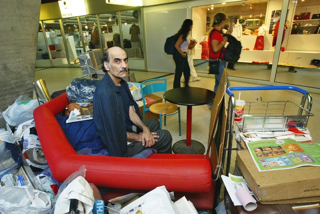 Iranian refugee, Nasseri is sat Charles De Gaulle airport surrounded by his belongings which include various items in bags
