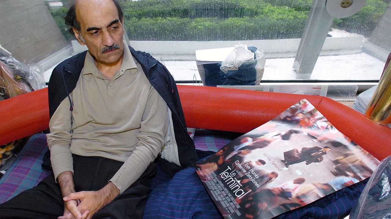 Iranian Refugee Nasseri sits next to a poster promoting 'The Terminal' - a film inspired by him