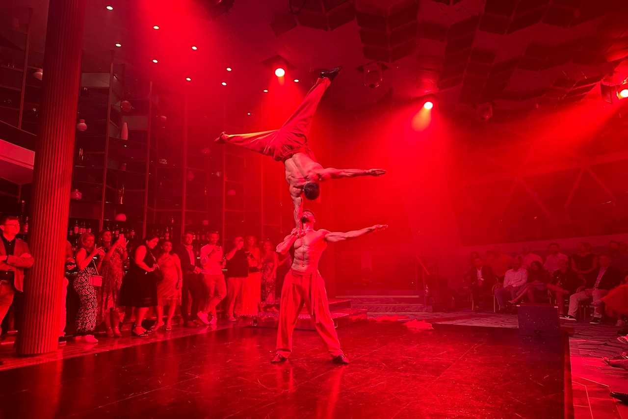 Two acrobats doing head balancing with red lighting in front of an audience during a show on a cruise ship