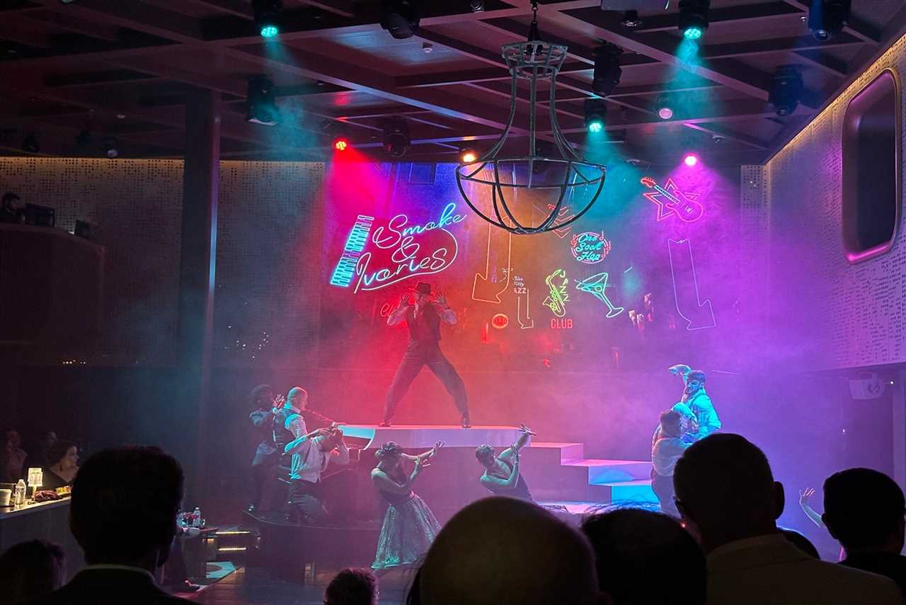 A group of singers and dancers on stage among rainbow slights with a crowd in front