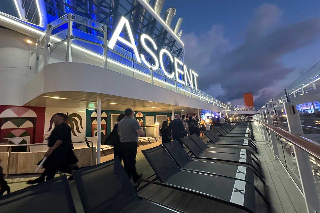 A cruise ship promenade deck with a lit sign above it bearing the shps name, Ascent