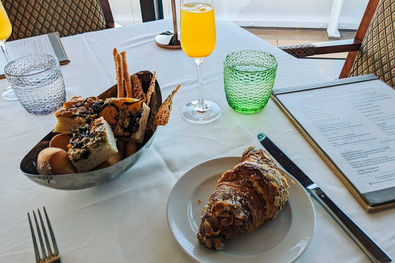 Bread basket and almond croissant with mimosa on cruise ship table overlooking the sea