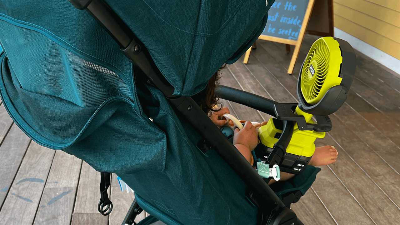 A toddler sitting in a stroller with a Ryobi fan