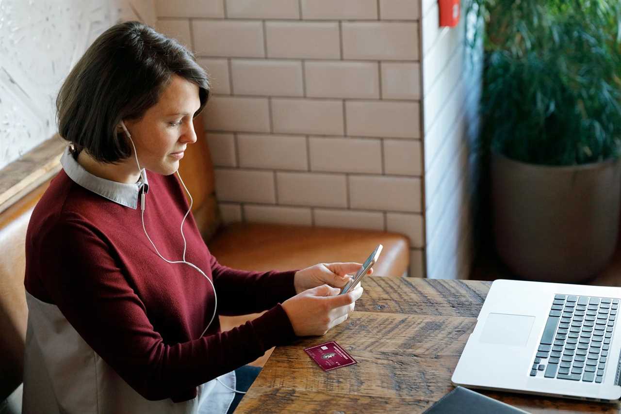 Young woman sitting looking at her phone while wearing earbuds